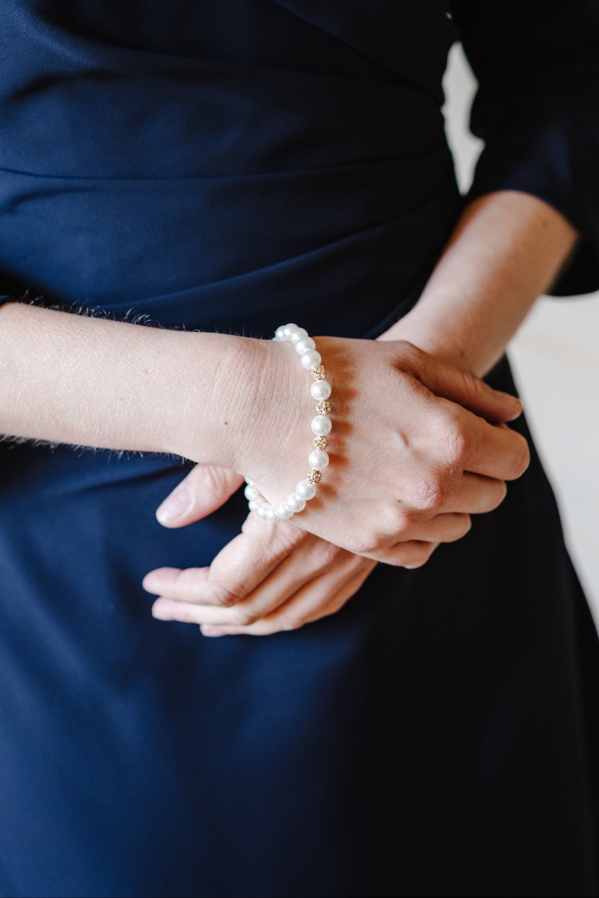 Person wearing a navy blue dress with a pearl bracelet on a neutral background