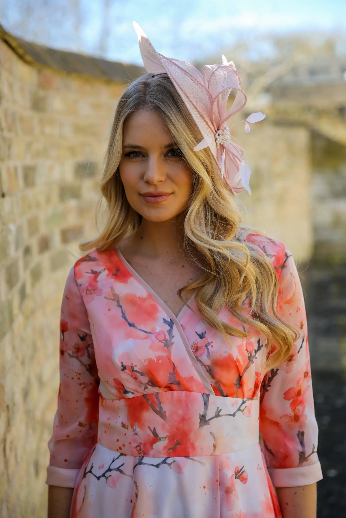 A woman wearing a pink and floral dress with a pink fascinator hat adorned with crystal details and feathers.