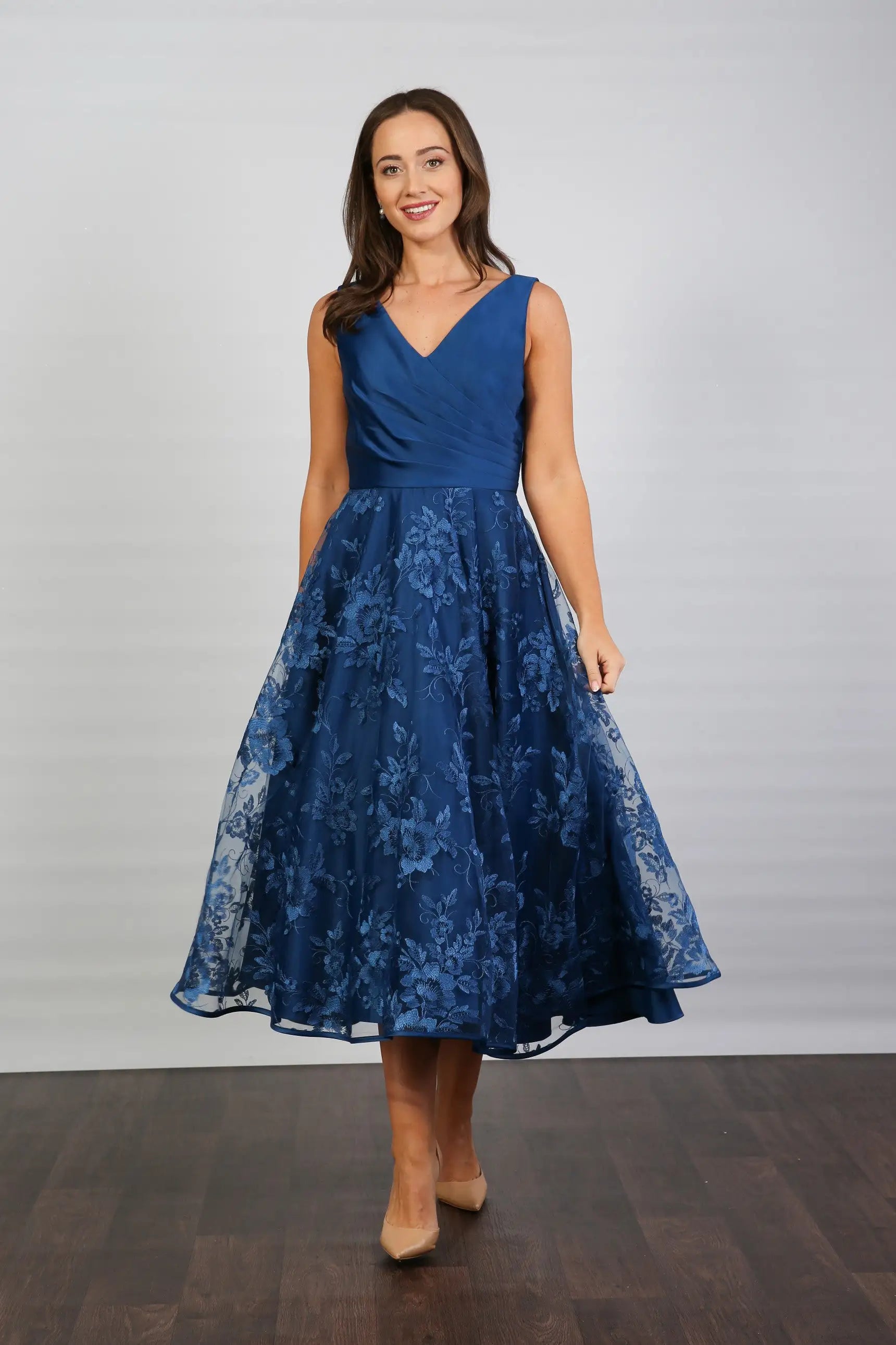 A woman wearing an elegant sleeveless midi length dress with a v-neck and fully lined embroidered skirt in Oxford Blue.