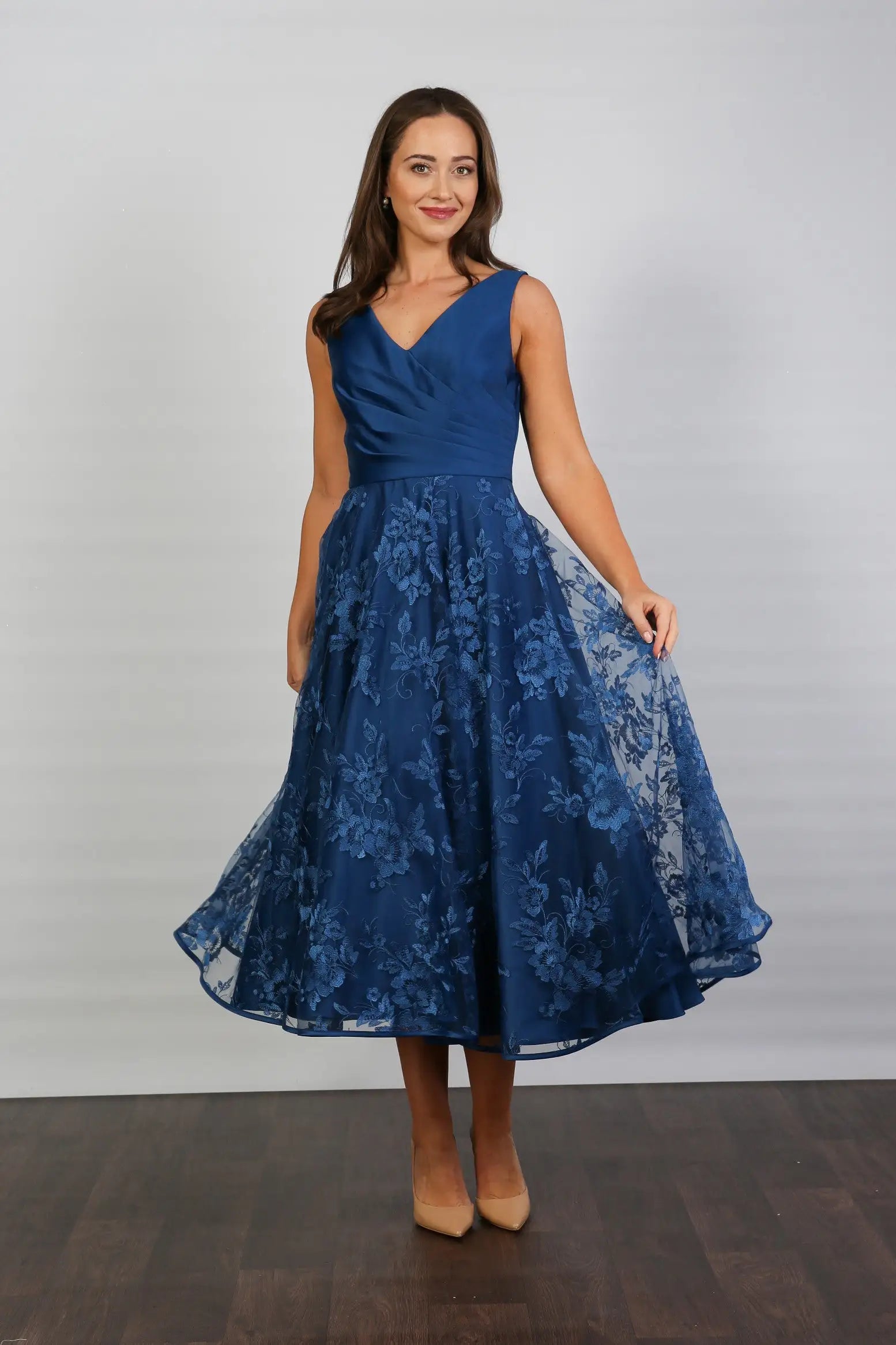 A woman wearing an elegant sleeveless midi length dress with a v-neck and fully lined embroidered skirt in Oxford Blue.