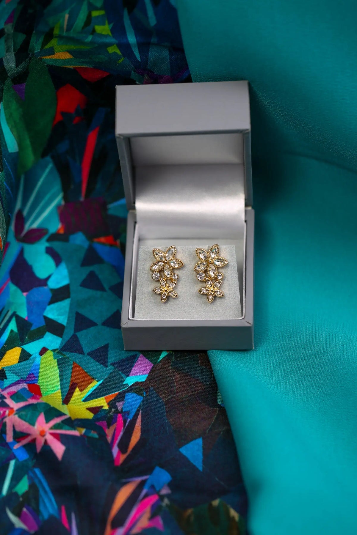 Gold floral earrings in a silver box on a colorful fabric background