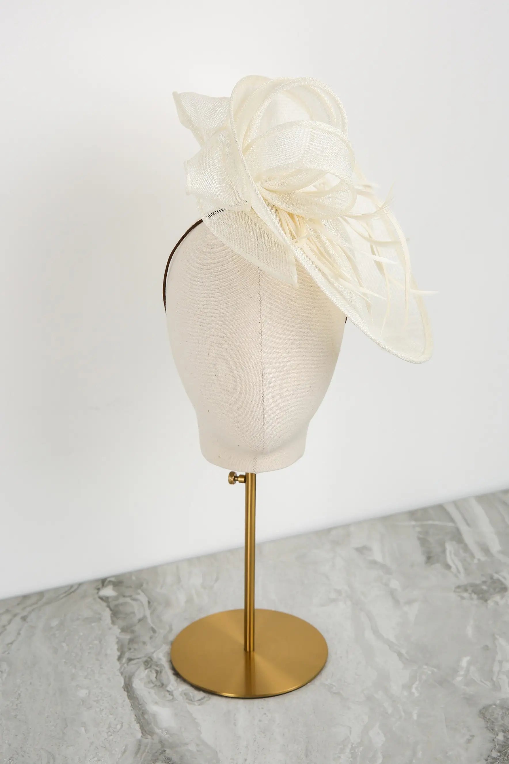 White fascinator on a mannequin head with a gold stand against a white background