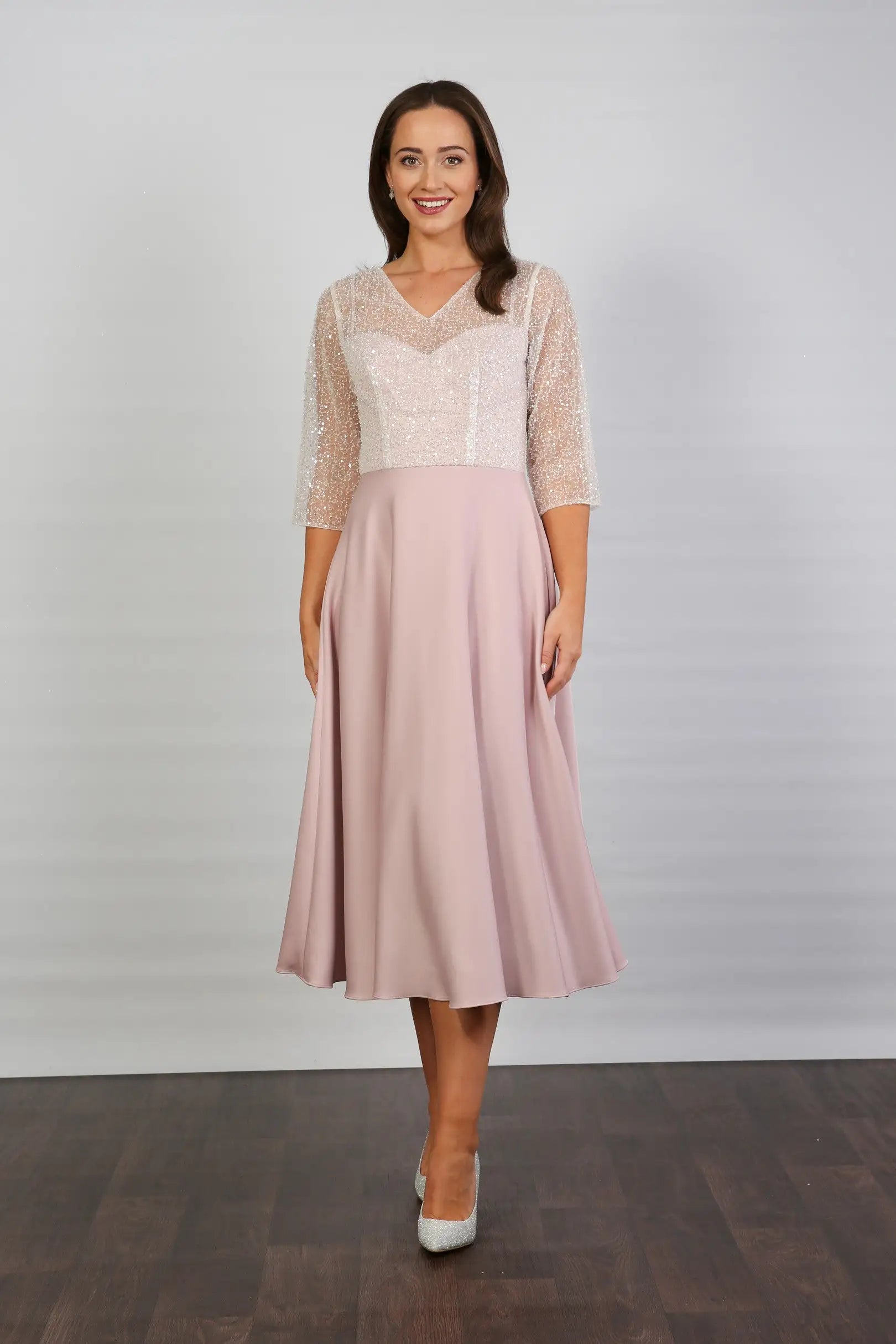 A woman models a blush-coloured, midi-length, beaded special occasion dress with a sweetheart neckline and 3/4 sleeves.