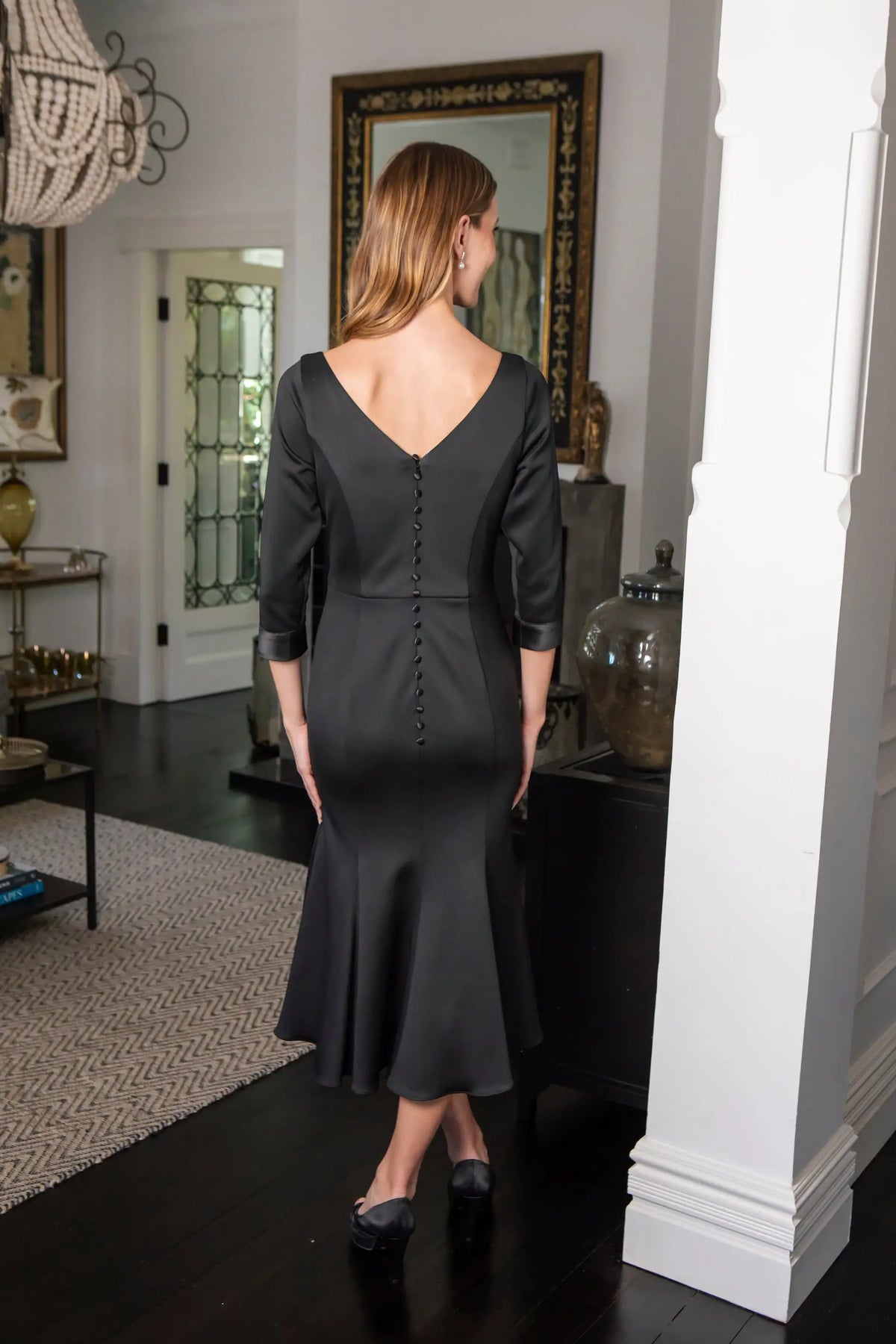 Woman wearing a black dress standing in a room with a mirror and decor.