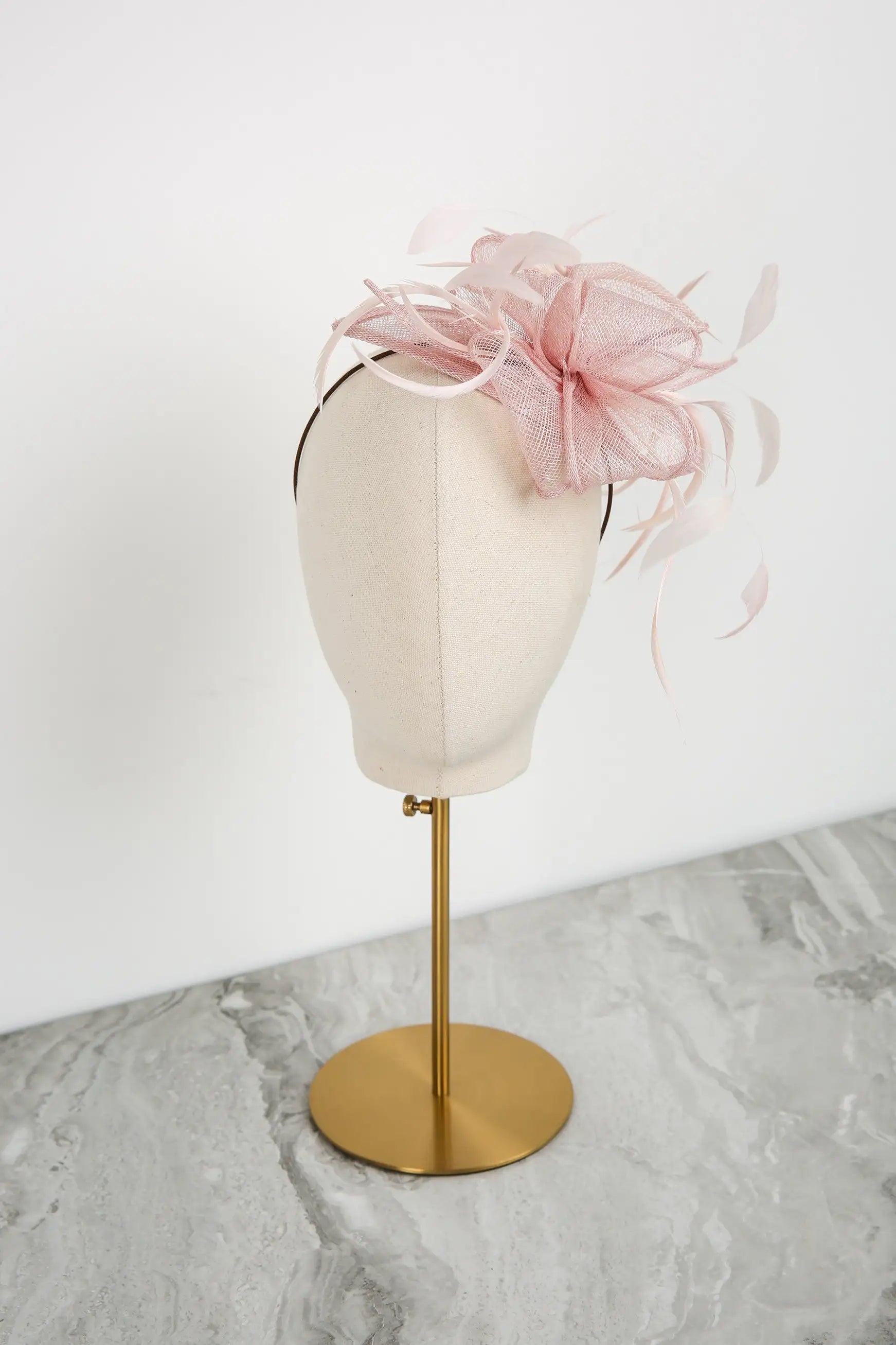 Pink fascinator on a mannequin head with a gold stand against a white background