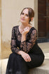 A woman wearing a black ankle-length evening dress with long sleeves and textured lace detailing.
