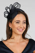 A woman wearing a navy fascinator with loops of sinamay and a small hand made flower to the right.