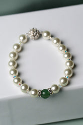 A pearl beaded bracelet with a green round bead and silver-toned metal accents, displayed on a white gift box against a soft mint green background.