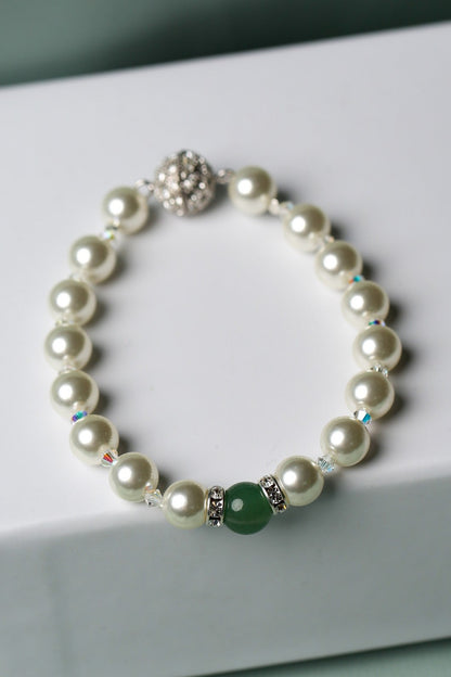 A pearl beaded bracelet with a green round bead and silver-toned metal accents, displayed on a white gift box against a soft mint green background.