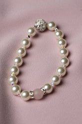 A pearl beaded bracelet with a silver-toned round clasp and a pink accent bead, displayed on a soft pink satin fabric background.