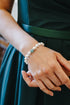 A close-up of a person wearing a dark teal green satin dress with a matching waistband, showcasing a white pearl beaded bracelet with a small green stone on their wrist.