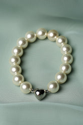 A pearl beaded bracelet with a polished silver heart charm, displayed on a draped mint green fabric background.