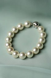 A pearl beaded bracelet with a polished silver clasp, resting on a textured light green fabric background.