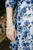 A close-up lifestyle shot of a woman wearing a white pearl bracelet with a small silver heart charm, paired with a blue and white floral dress.