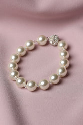 A pearl beaded bracelet with a silver-toned rhinestone-embellished clasp, displayed on a soft pink satin fabric background.