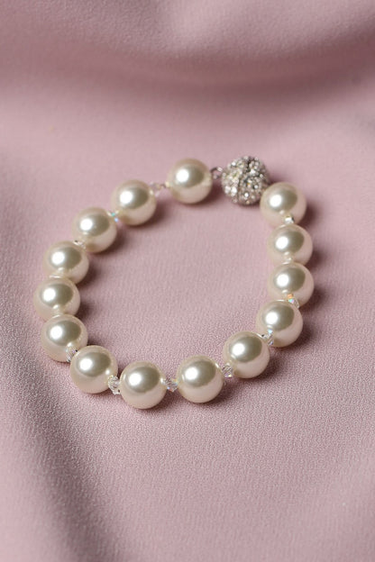 A pearl beaded bracelet with a silver-toned rhinestone-embellished clasp, displayed on a soft pink satin fabric background.