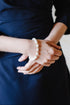 Person wearing a navy blue dress with a pearl bracelet on a neutral background