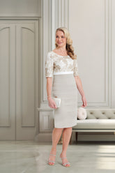 Woman in a white dress with floral lace details standing in a room with a couch and decorative items.