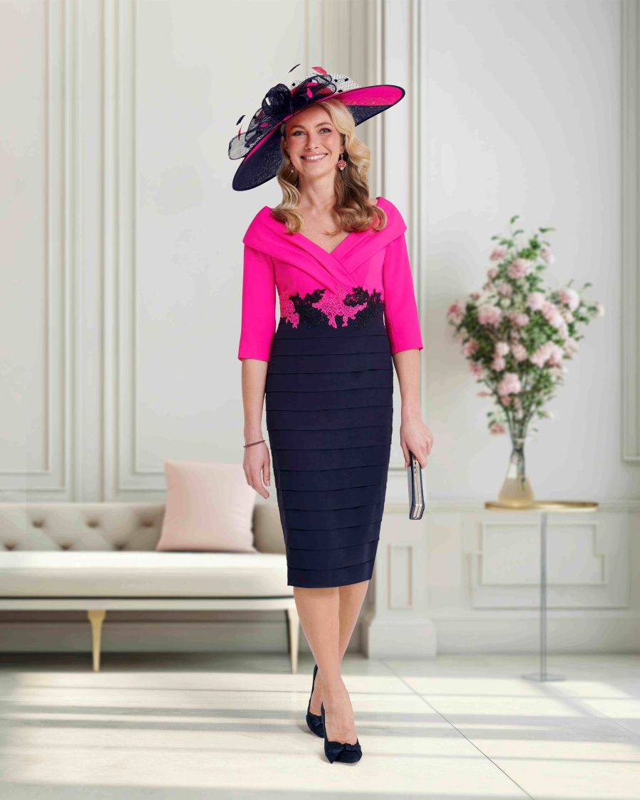 Woman wearing a pink and navy dress with a matching hat in an elegant room.