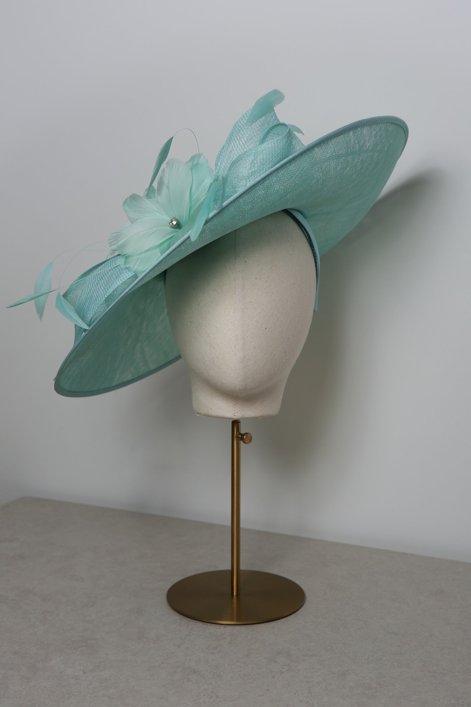 Seafoam hat with decorative elements on a mannequin head against a plain background