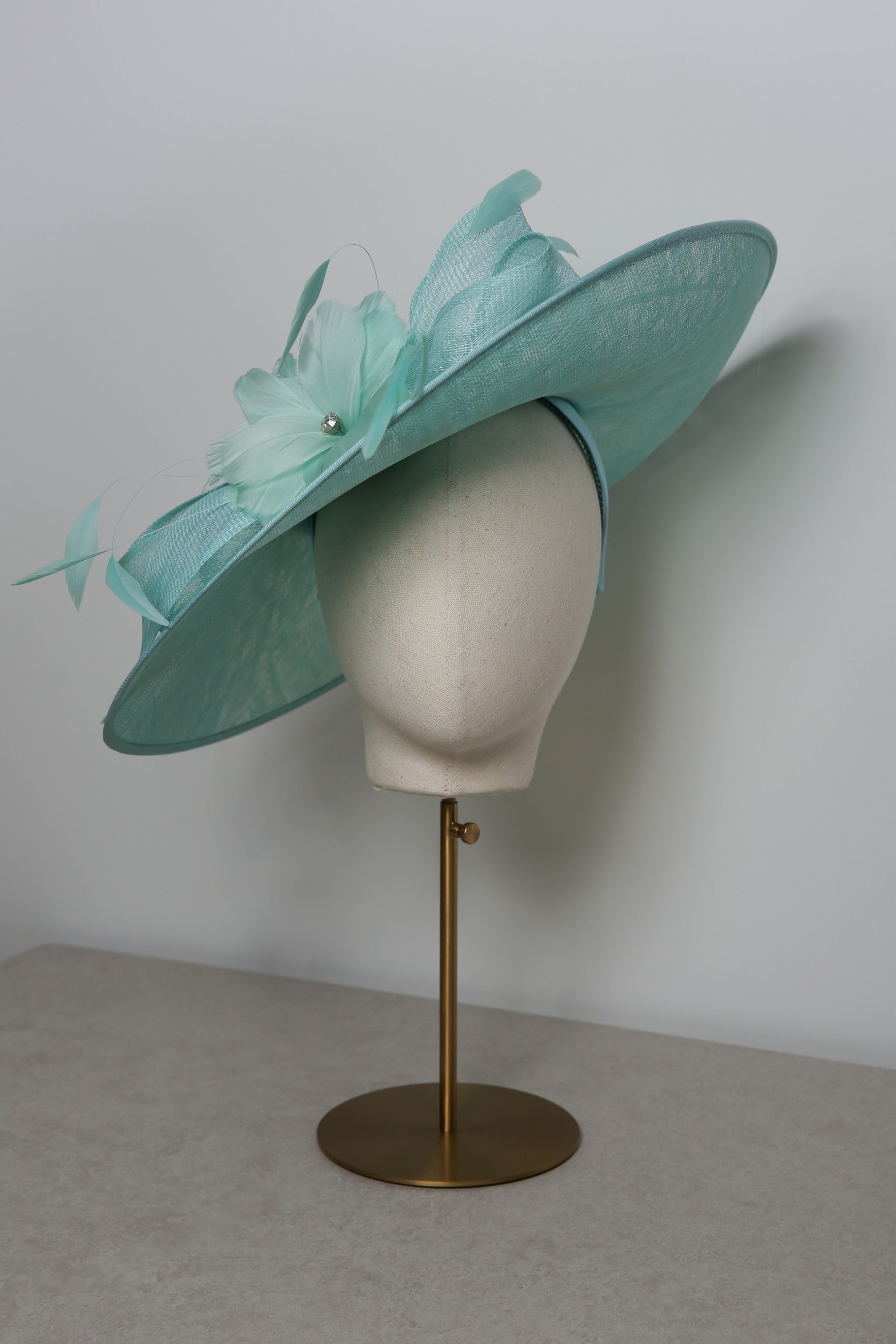 Seafoam hat with decorative elements on a mannequin head against a plain background