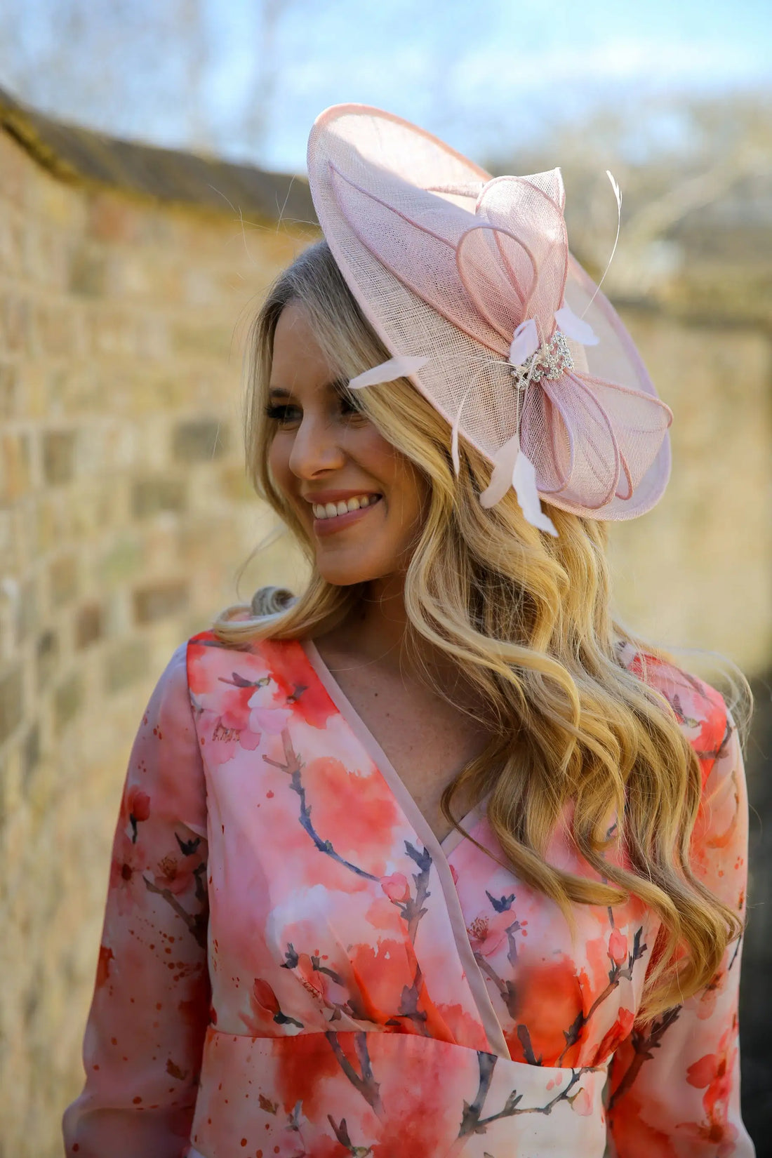 A woman wearing a pink and floral dress with a pink fascinator hat adorned with crystal details and feathers.