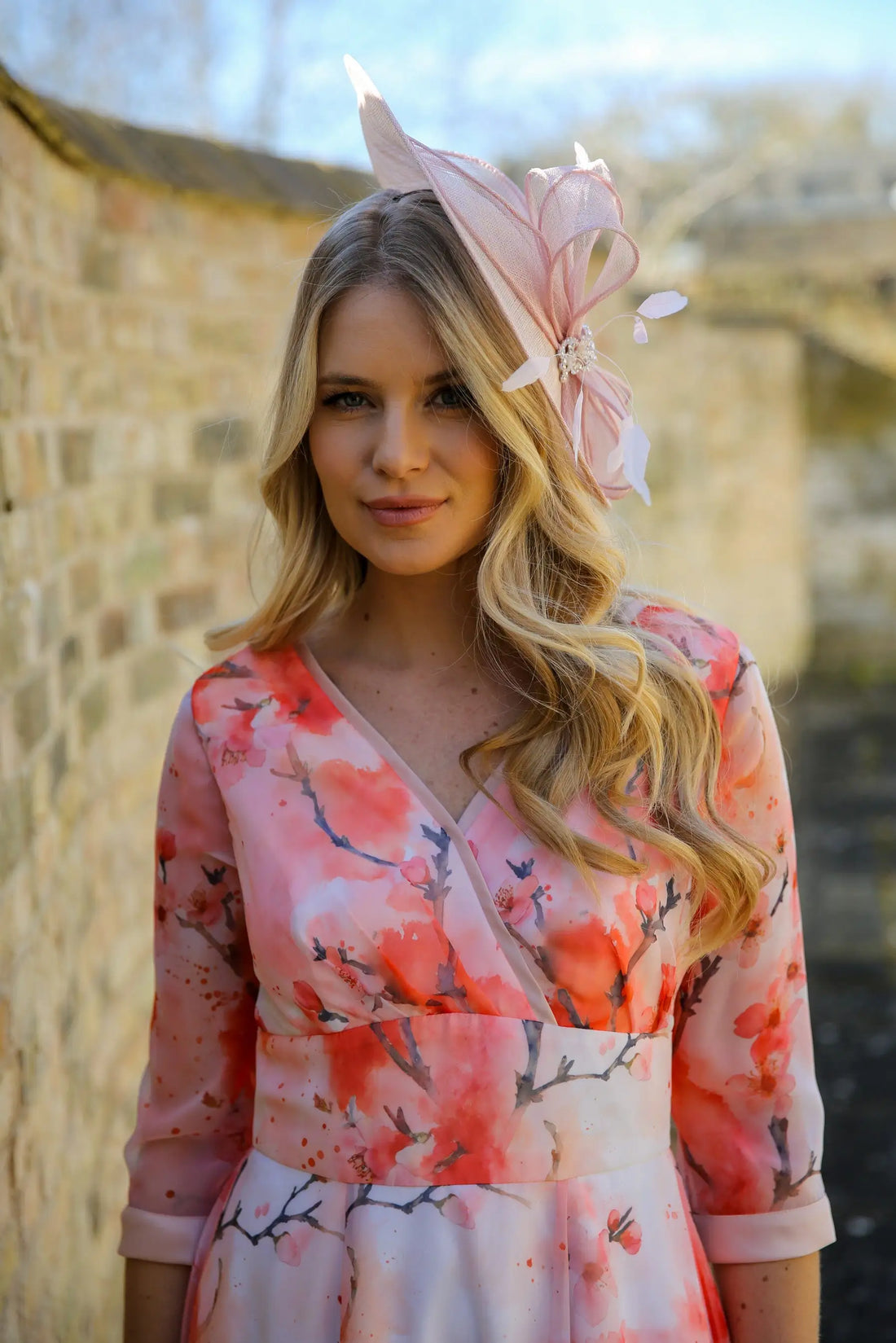 A woman wearing a pink and floral dress with a pink fascinator hat adorned with crystal details and feathers.