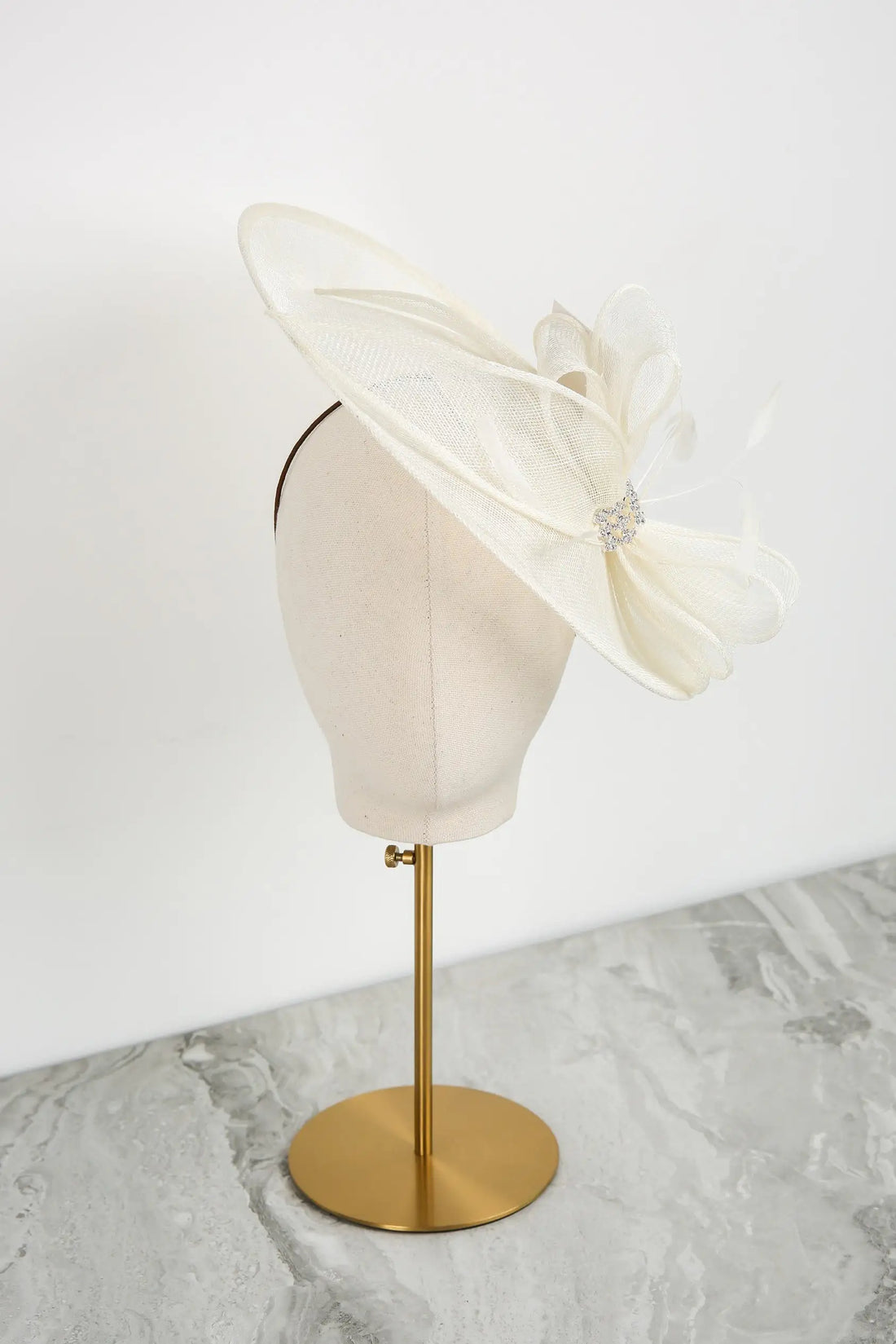 White decorative headpiece on a mannequin head with a gold stand against a white background