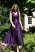 A woman wearing a sleeveless, midi-length blackberry purple dress with embroidery on the skirt.