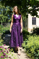 A woman wearing a sleeveless, midi-length blackberry purple dress with embroidery on the skirt.