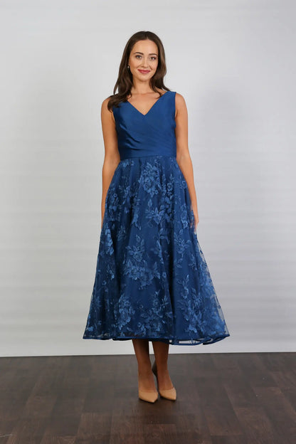 A woman wearing an elegant sleeveless midi length dress with a v-neck and fully lined embroidered skirt in Oxford Blue.