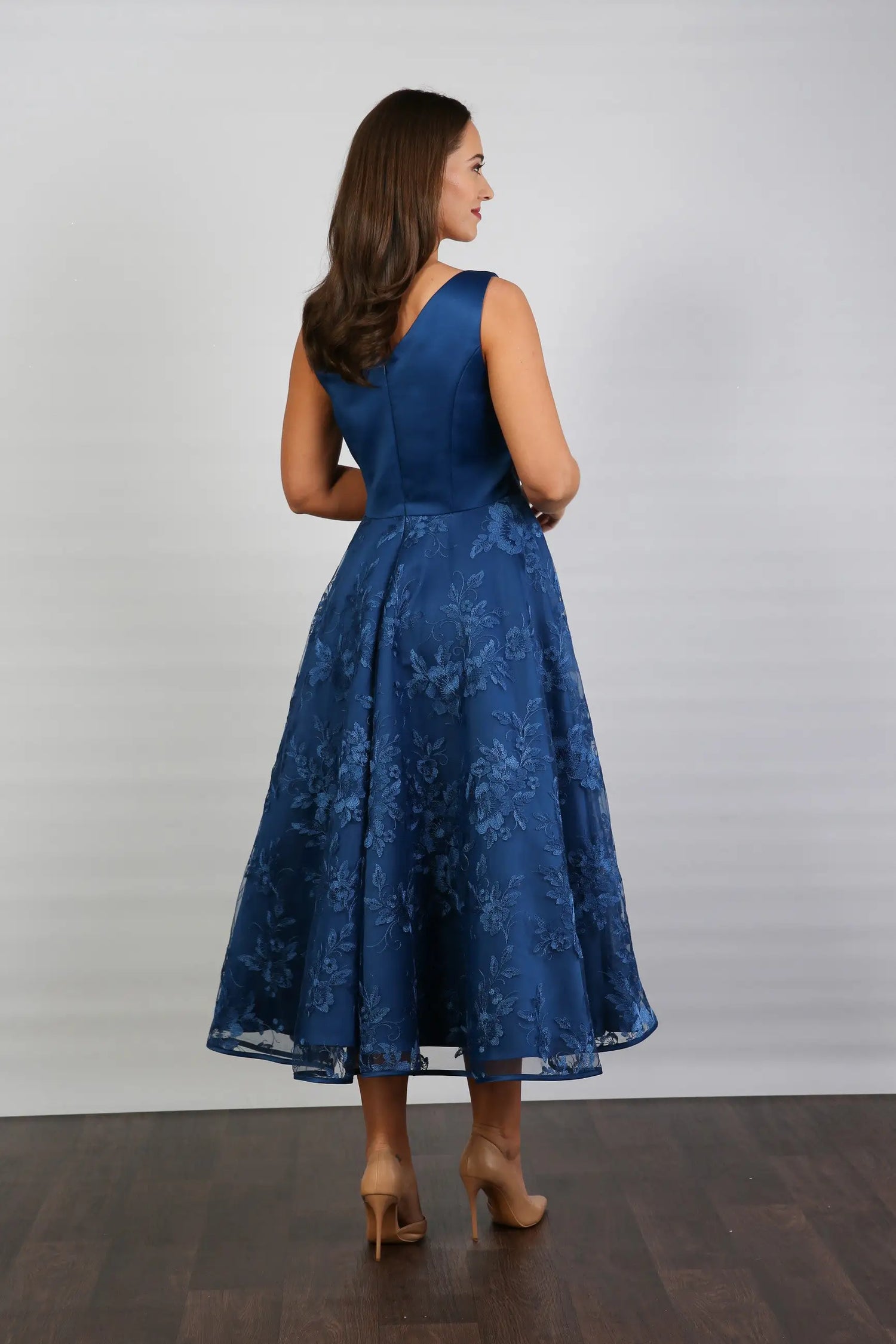 A woman wearing an elegant sleeveless midi length dress with a v-neck and fully lined embroidered skirt in Oxford Blue.