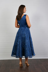 A woman wearing an elegant sleeveless midi length dress with a v-neck and fully lined embroidered skirt in Oxford Blue.