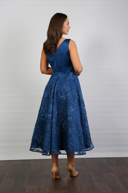 A woman wearing an elegant sleeveless midi length dress with a v-neck and fully lined embroidered skirt in Oxford Blue.