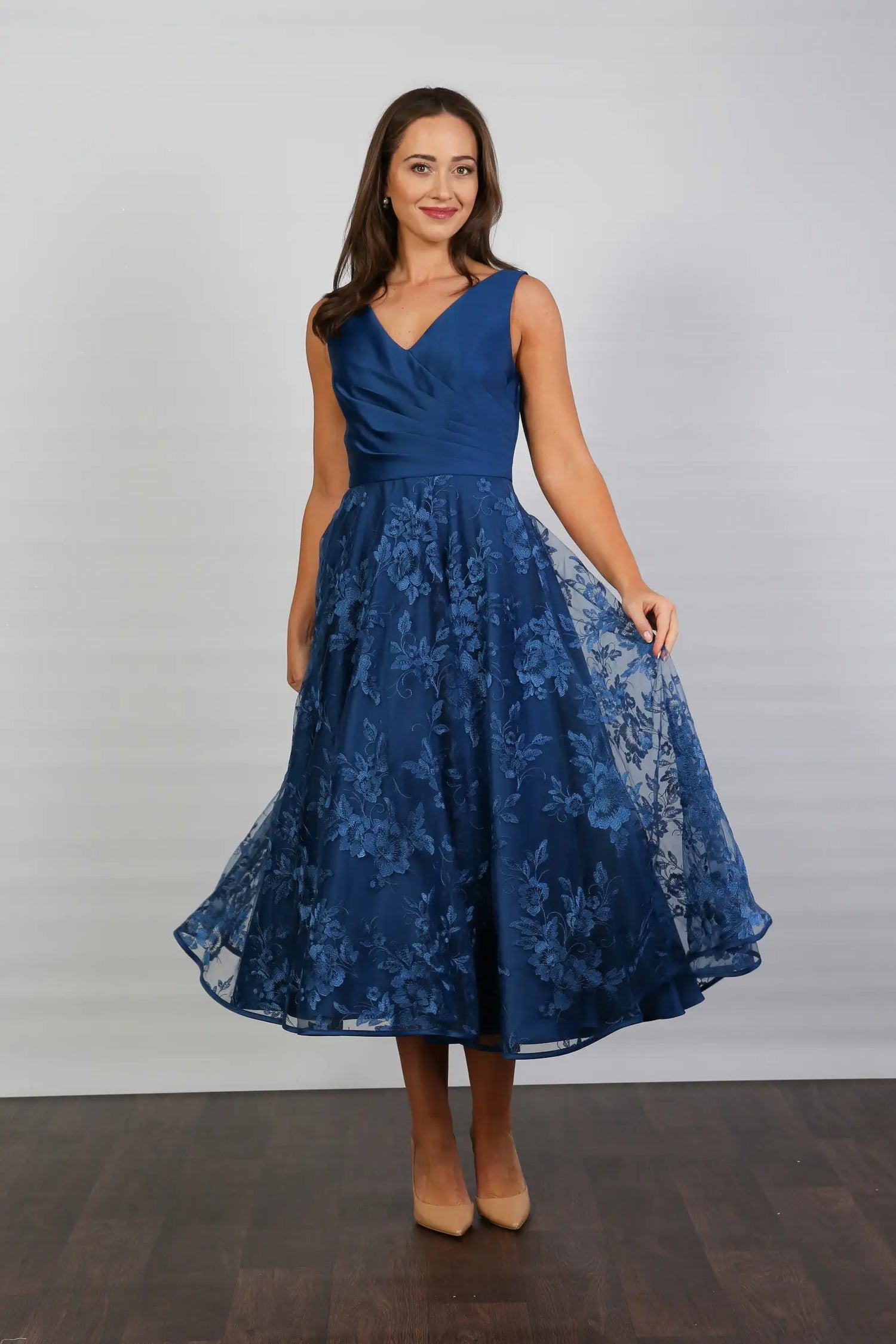 A woman wearing an elegant sleeveless midi length dress with a v-neck and fully lined embroidered skirt in Oxford Blue.