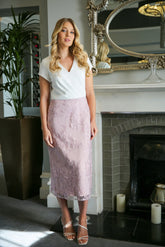 A woman wearing a blush pink midi dress with embroidery over the skirt and a v-neckline.