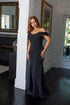 Woman in a black off-shoulder gown standing in a room with mirrors and a door.