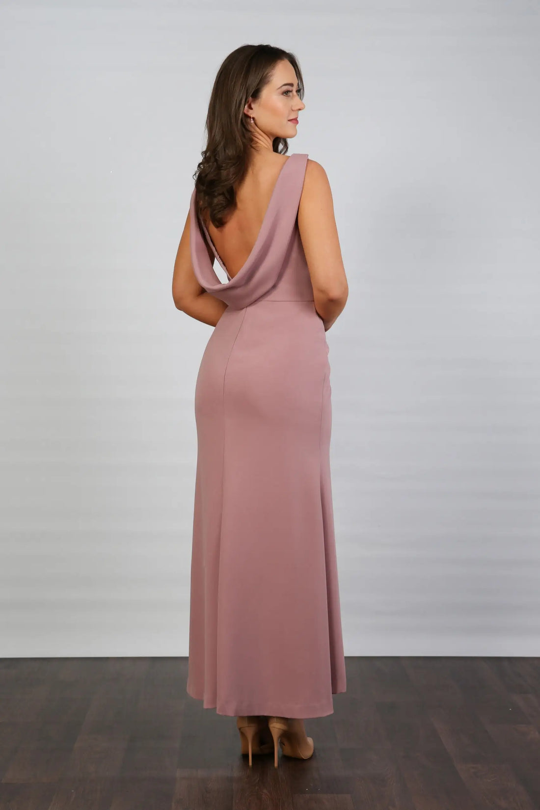 A model wearing a sleeveless, V-neck, dusty rose maxi dress with a deep cowl back and pleated waist, suitable for day to evening events.