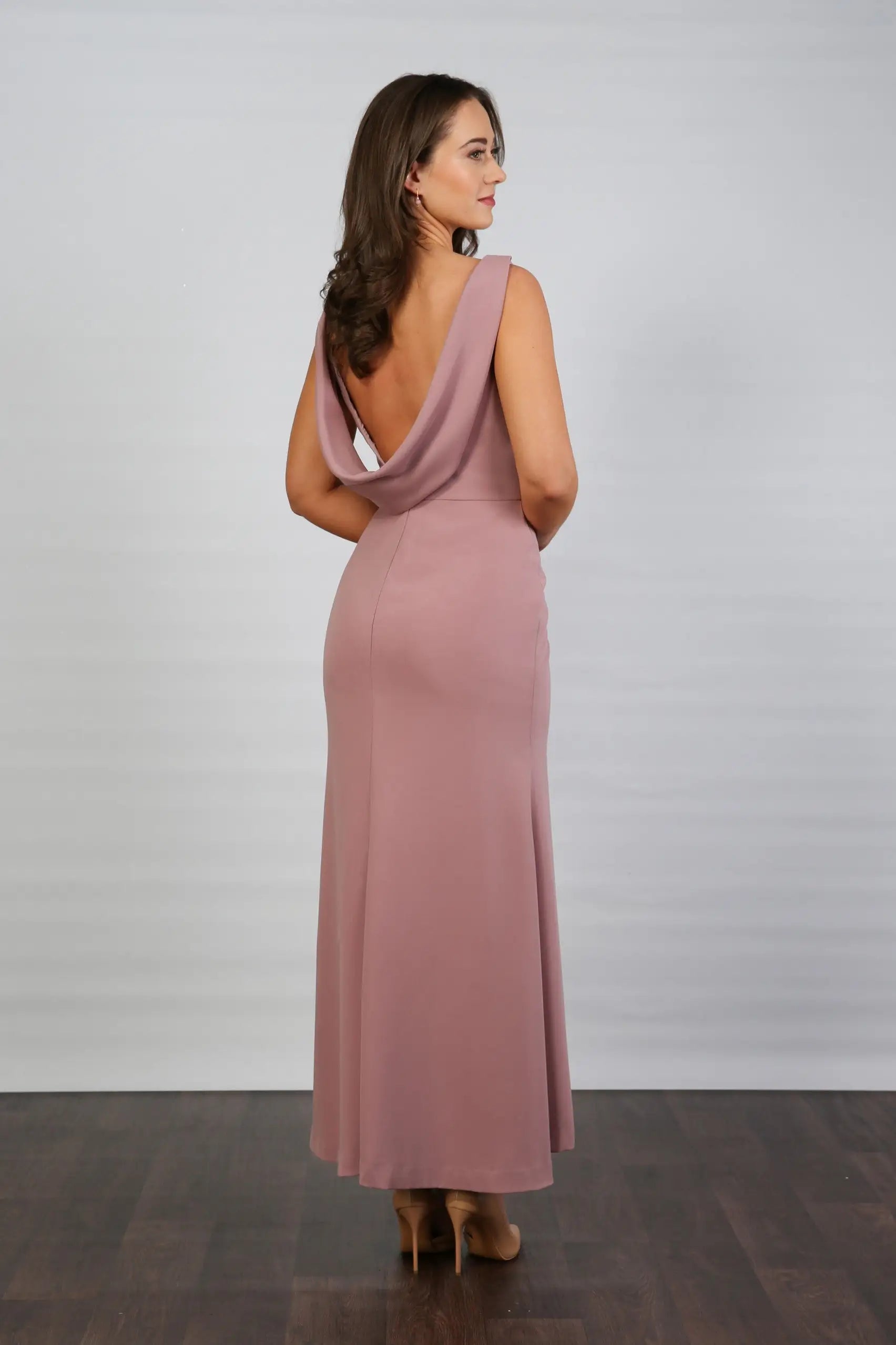 A model wearing a sleeveless, V-neck, dusty rose maxi dress with a deep cowl back and pleated waist, suitable for day to evening events.