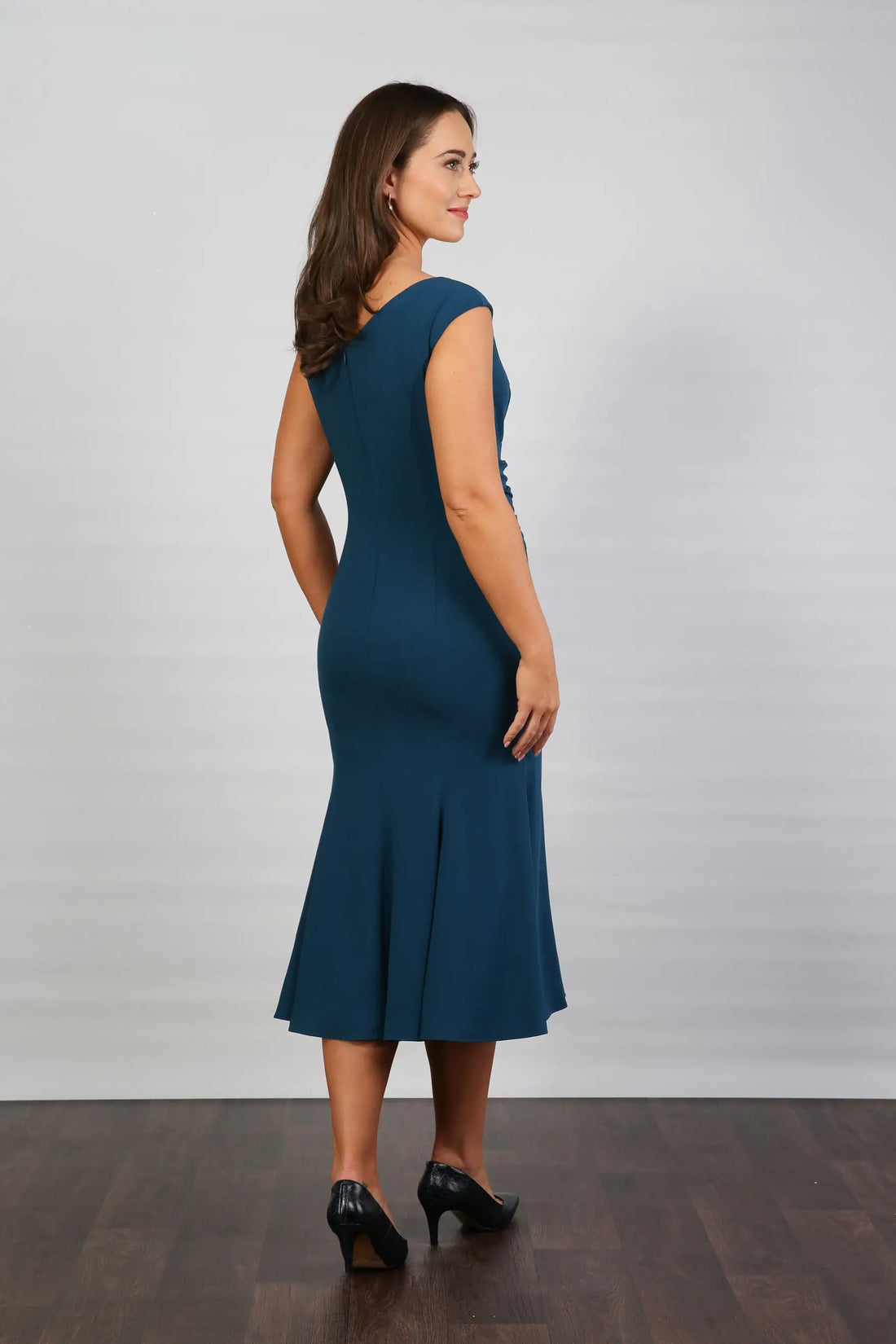 A woman models the Carla Moss Crepe Dress in Ocean, a sleeveless, v-neck, fit and flare dress with a mid-length design.