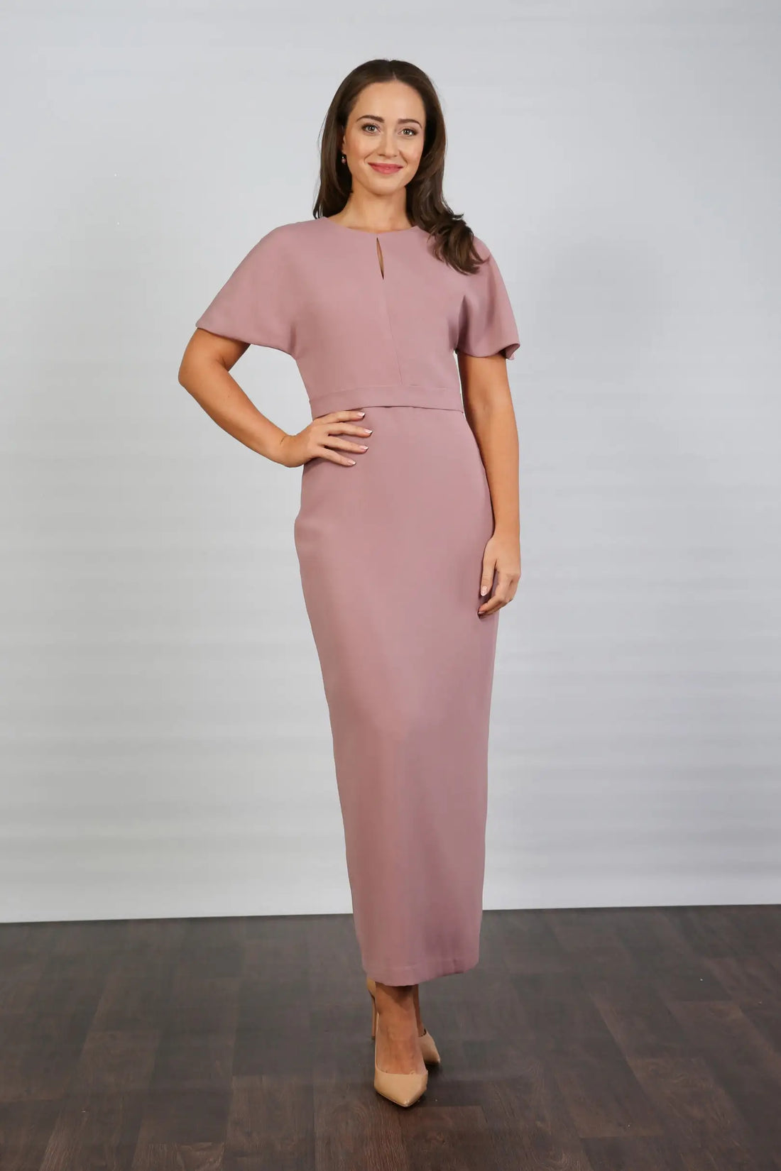 A woman models an ankle-length dress in a dusty rose colour, featuring a round neckline, short sleeves, and a back zip fastening.