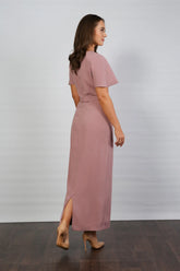 A woman models an ankle-length dress in a dusty rose colour, featuring a round neckline, short sleeves, and a back zip fastening.