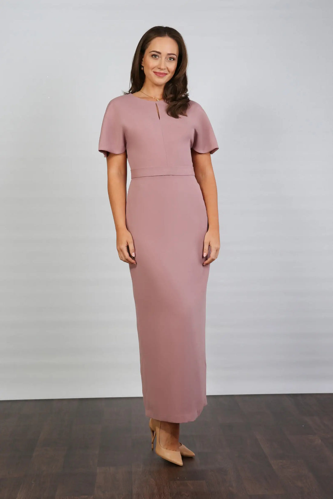 A woman models an ankle-length dress in a dusty rose colour, featuring a round neckline, short sleeves, and a back zip fastening.