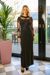 A woman in a long black evening dress with long sleeves and embroidery.