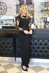 A woman in a long black evening dress with long sleeves and embroidery.