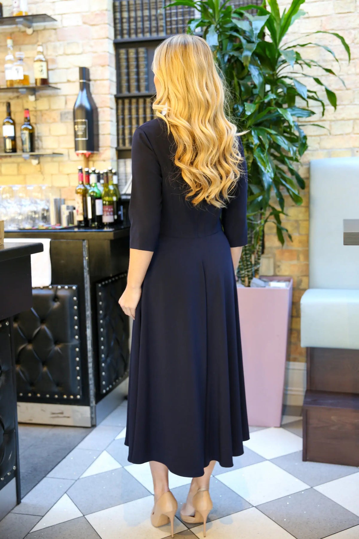 A model wearing a dark navy, midi length, v-neck crepe dress with a full skirt and elbow-length sleeves.