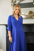 A woman wearing an electric blue, v-neck, midi length crepe dress with a fitted waist and 3/4 sleeves.