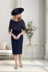 Woman in a navy dress with a matching hat standing in a well-lit room with a vase of flowers.