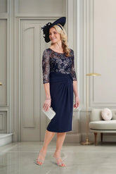 Woman in a navy dress with lace sleeves and a matching hat in an elegant room.