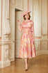 Woman in a floral dress and hat standing in an ornate room.